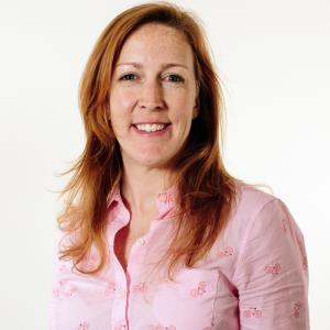A smiling woman with red hair and a pink shirt